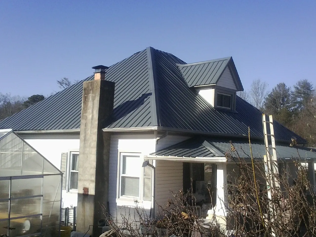 Dark blue standing seam metal roof on a white farmhouse with dormer — Slate & Tile Roof Repair by Roofing Brothers in Comfrey