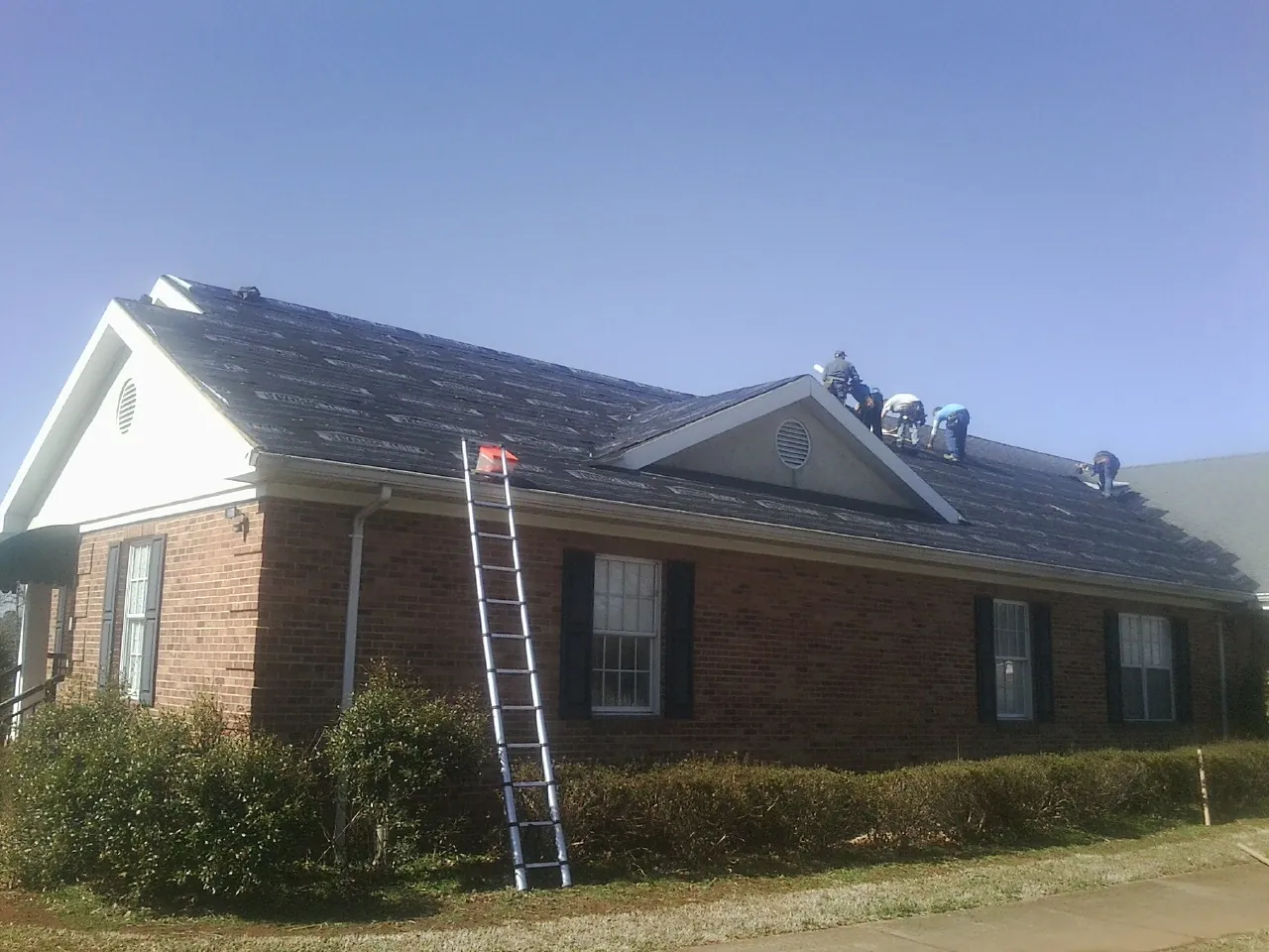 Crew tearing shingles off a brick ranch roof with a ladder set — Emergency Roof Repair work by our crew in Comfrey