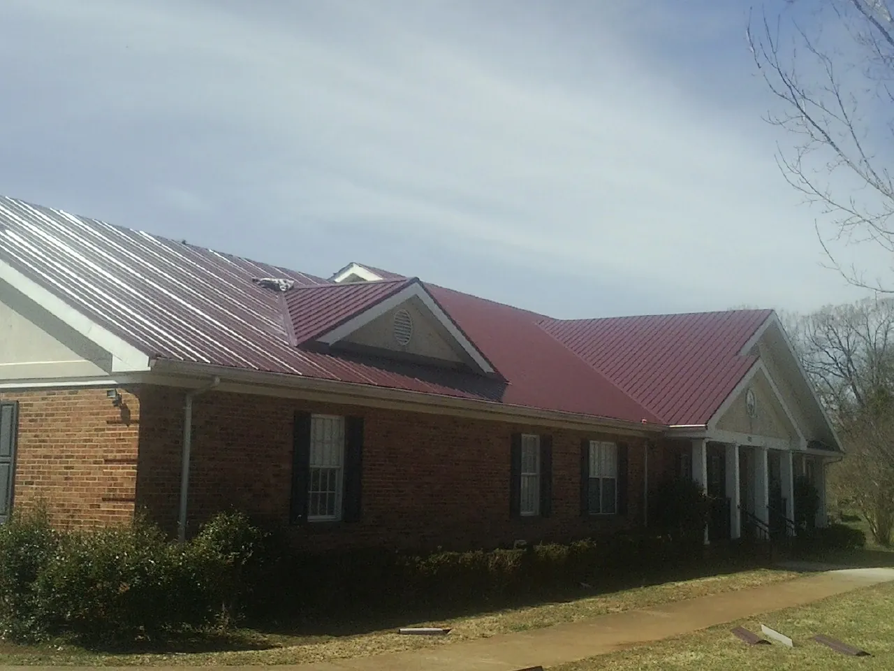 Red metal roof with gabled entries on a long brick building, from a Hail Damage Roof Repair job in Comfrey