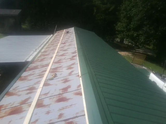 Old rusted panels beside newly installed green metal roofing — Wind Damage Roof Repair by Roofing Brothers in Comfrey