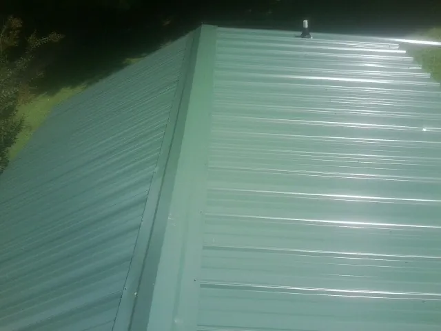 New green metal panels meeting at the ridge of a roof — Flat Roof Repair work by our crew in Comfrey