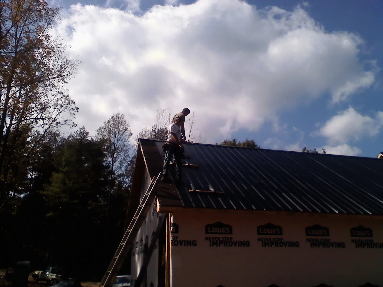 Roofer fastening dark metal panels high against a cloudy sky, from a Roof Inspection job in Comfrey
