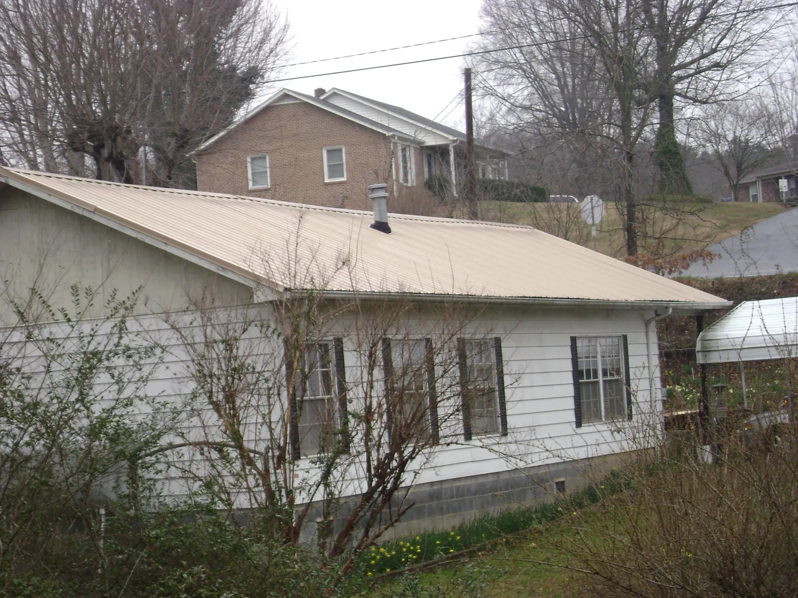 Tan metal roof on a white sided house set into a hillside — Commercial Roofing by Roofing Brothers in Comfrey