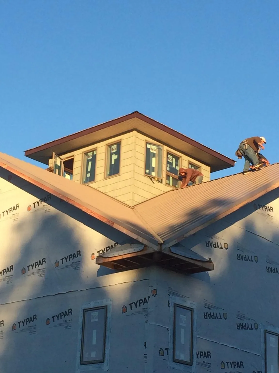Roofers working around a rooftop cupola on a new metal roof at sunset — Roof Waterproofing in Comfrey by Roofing Brothers
